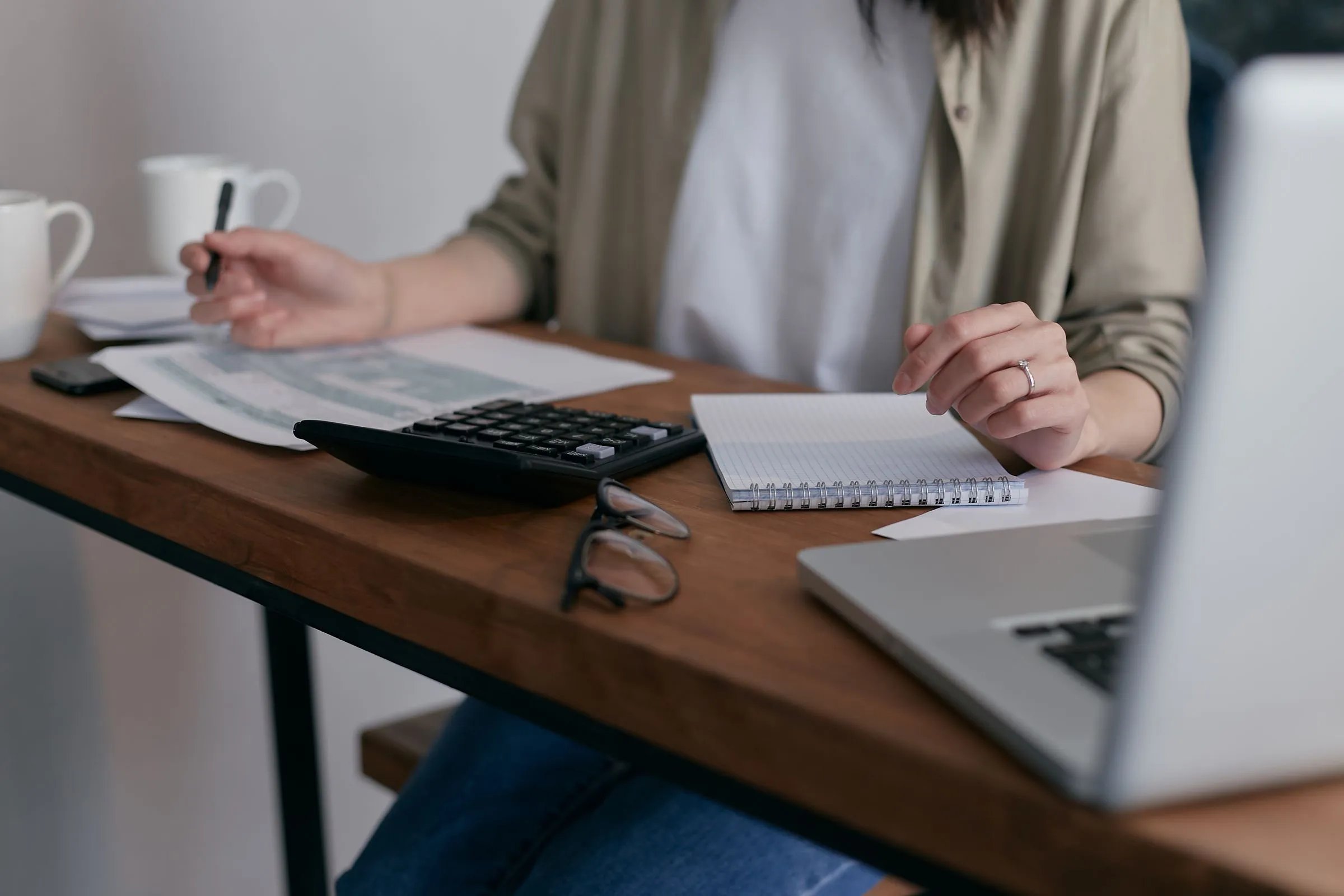 A person working on payroll paperwork beside a laptop