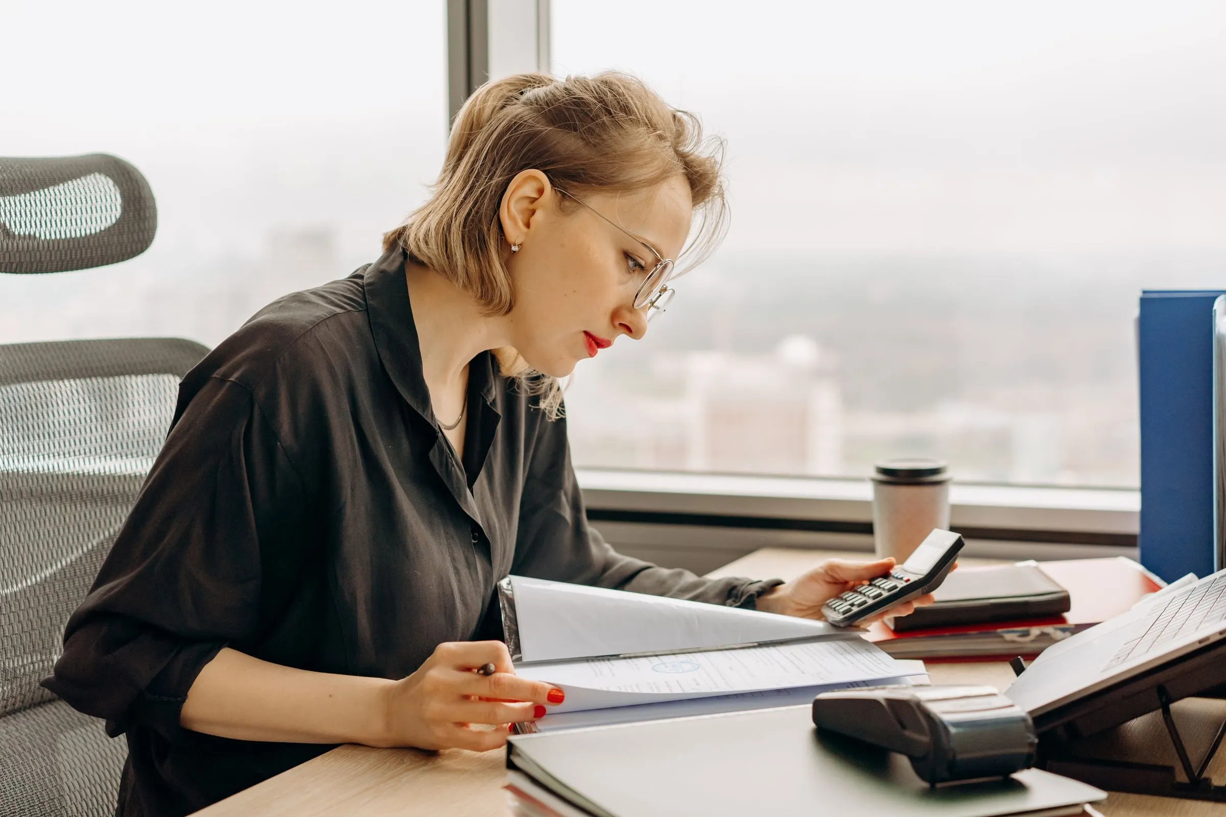 A professional reviewing financial papers with a calculator at an office desk
