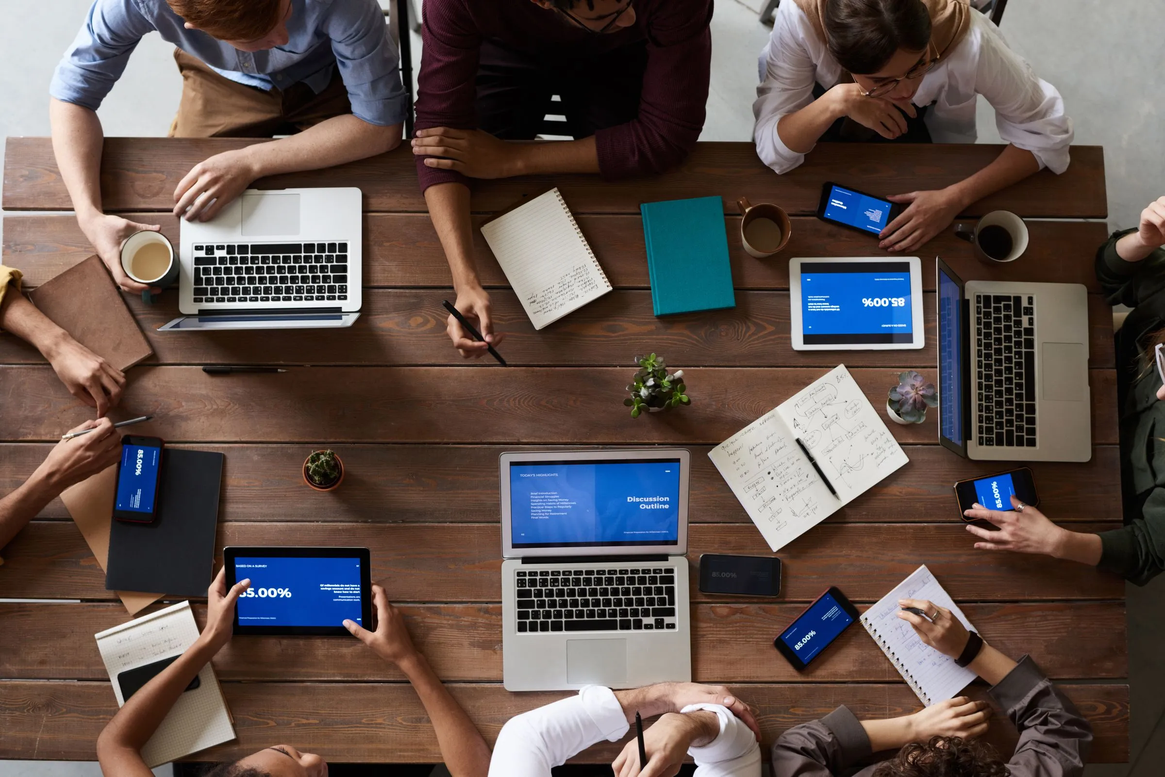 A team working with laptops and notebooks around a wooden table, seen from above